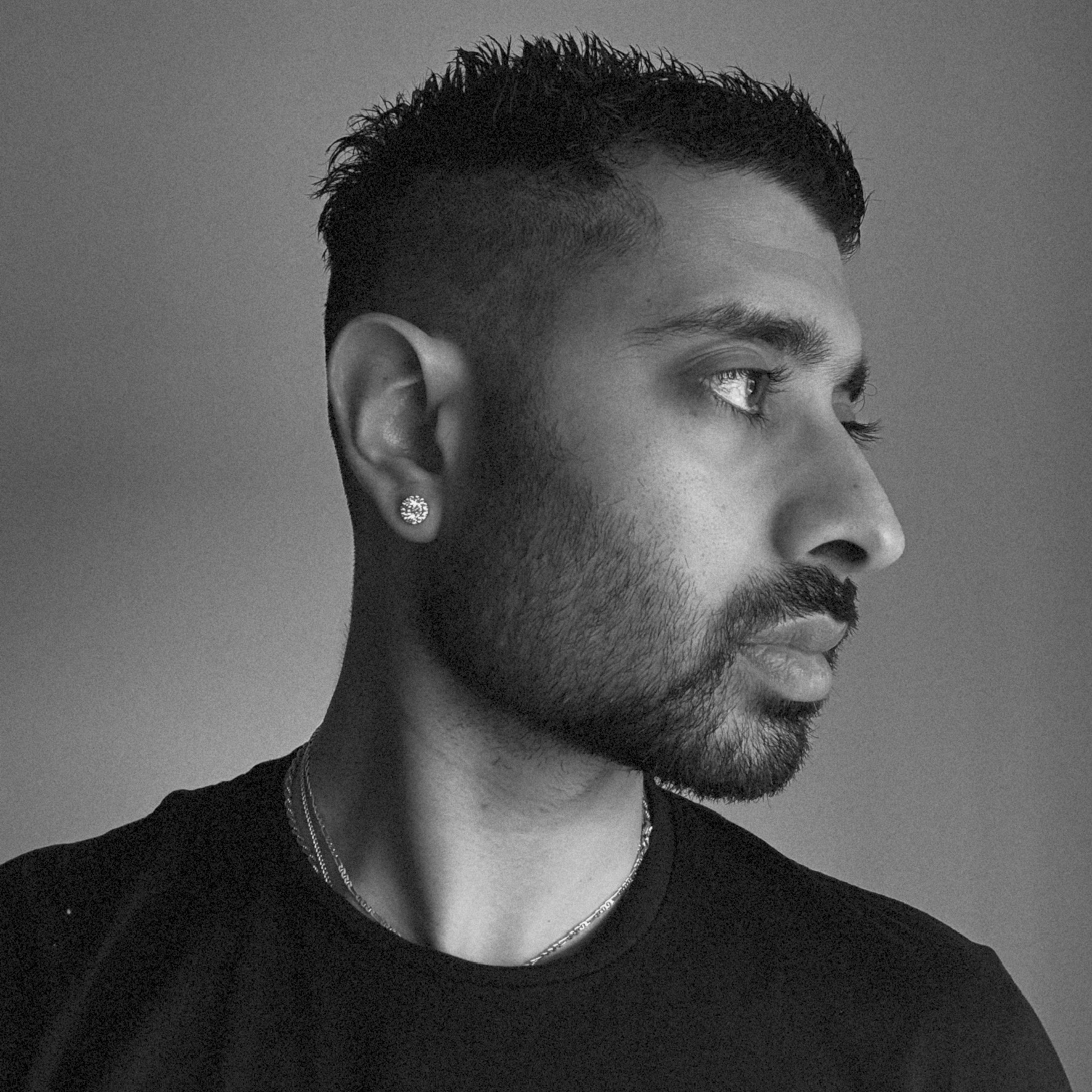 A side headshot of a young man with a beard looking to the side in black and white
